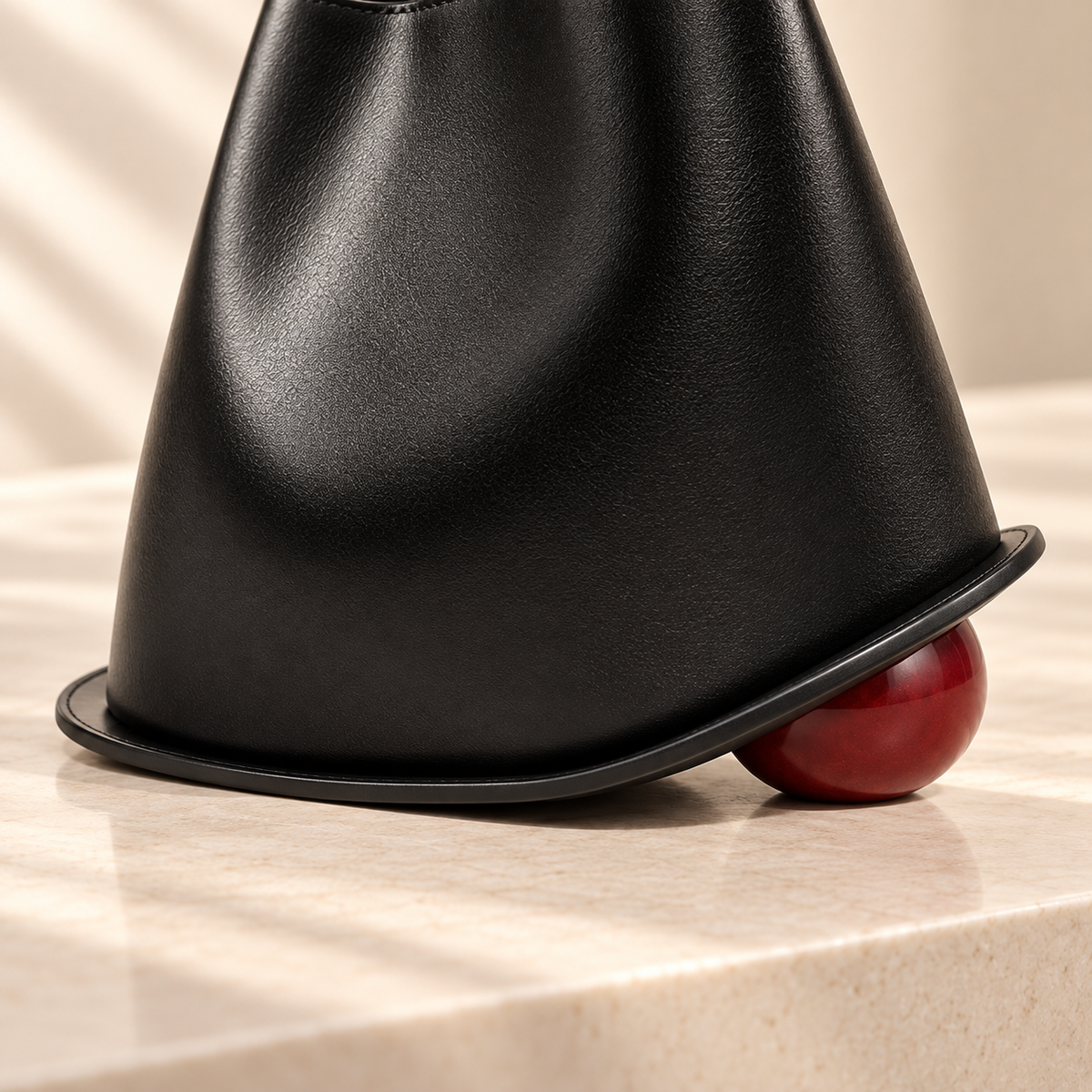 Détail de la base sculpturale et du pied sphérique bordeaux du Sac Signature Qavero noir